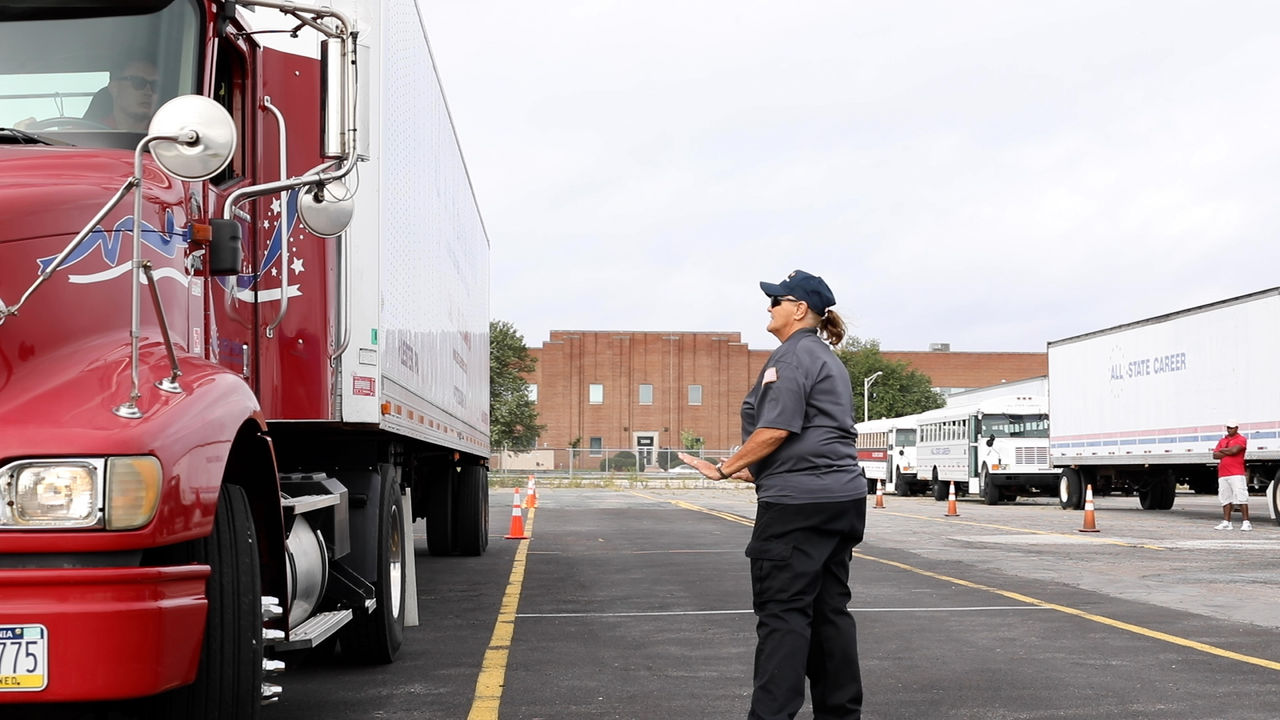 Female instructor guides red semi truck in parking lot